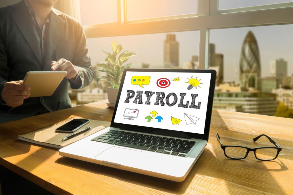 Laptop showing the word "payroll" on the screen with person standing next to it